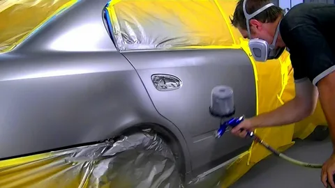 Car paint repair technician spray painting silver car door panel in Ajman workshop