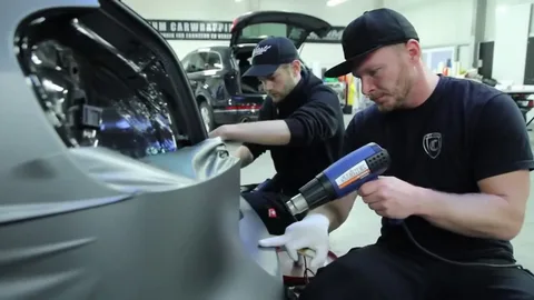 Professional installer applying vinyl wrap during car wrap vs paint installation process